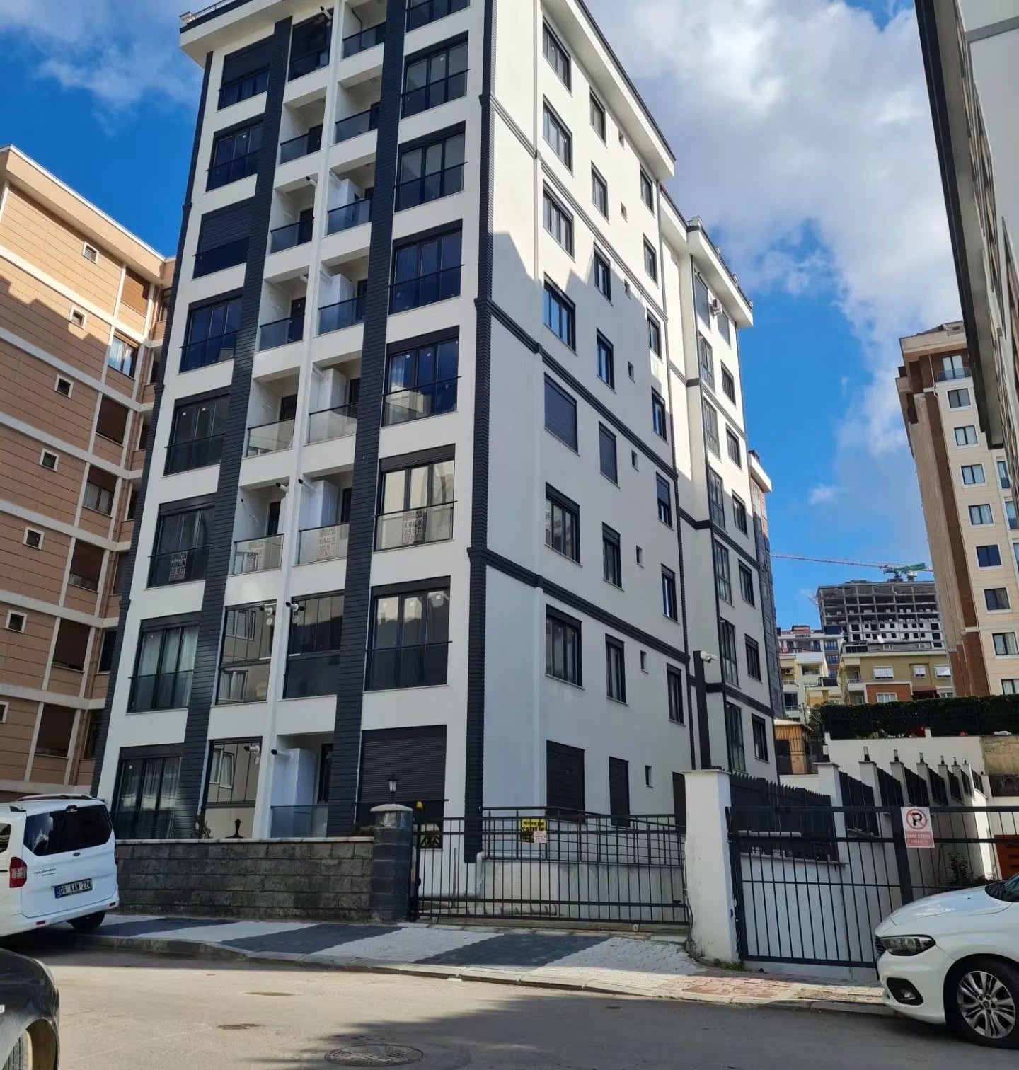 Tamamlanmış konut bloğunun sokaktan görünümü; beyaz ve antrasit cephe düzeni