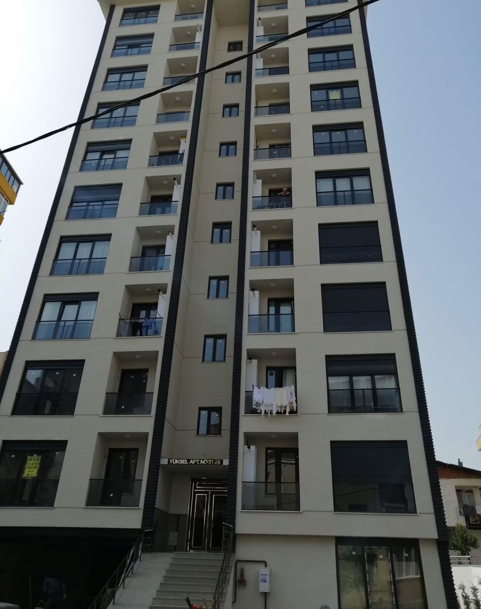 Tamamlanmış Yüksel Apartmanı’nın sokaktan yukarı bakışla çekilmiş cephe fotoğrafı; açık renkli kaplama ve kat boyunca balkonlar